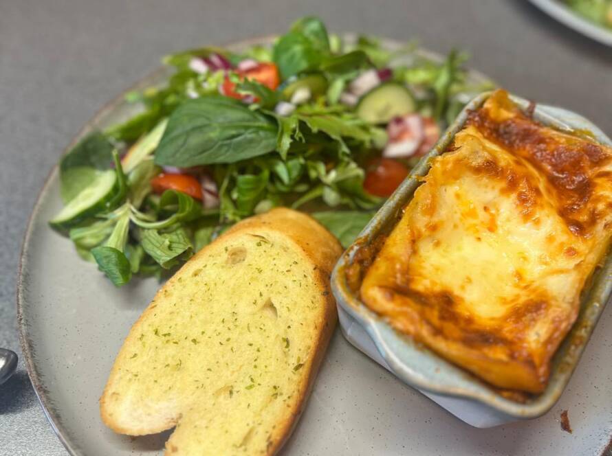 Homemade lasagna served with fresh salad and garlic bread at Mia’s Bakes & Cakes
