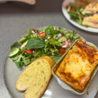 Homemade lasagna served with fresh salad and garlic bread at Mia’s Bakes & Cakes